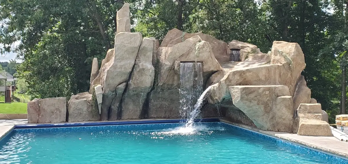 Towering sculpted waterfall spires above a residential pool with cascading water curtains