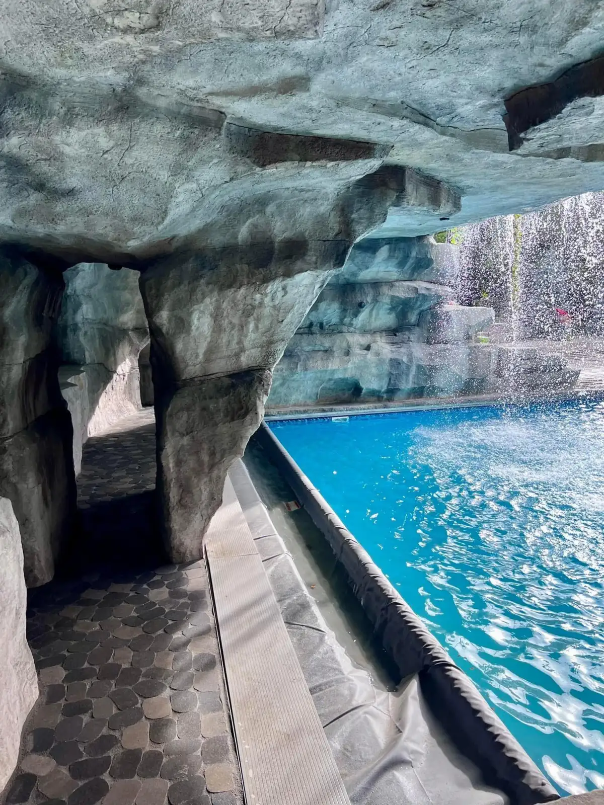 Walk-through pool grotto with overhead waterfall and integrated LED lighting